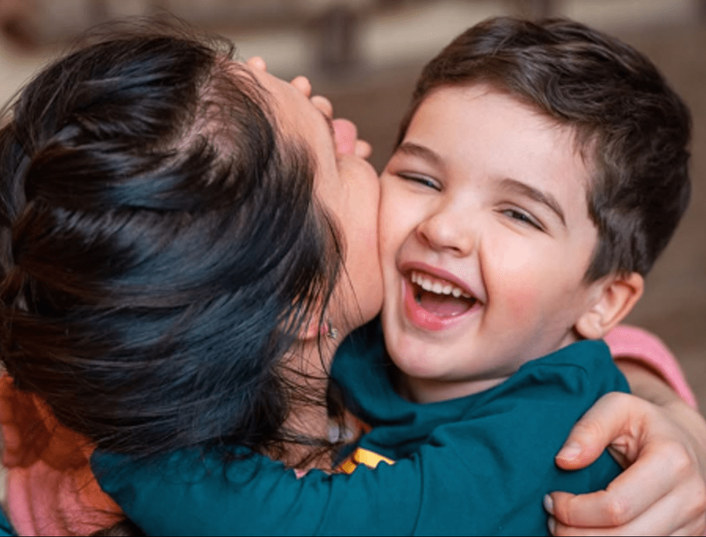 A joyful moment between a mother and her young son, as she kisses him on the cheek while he smiles happily.
