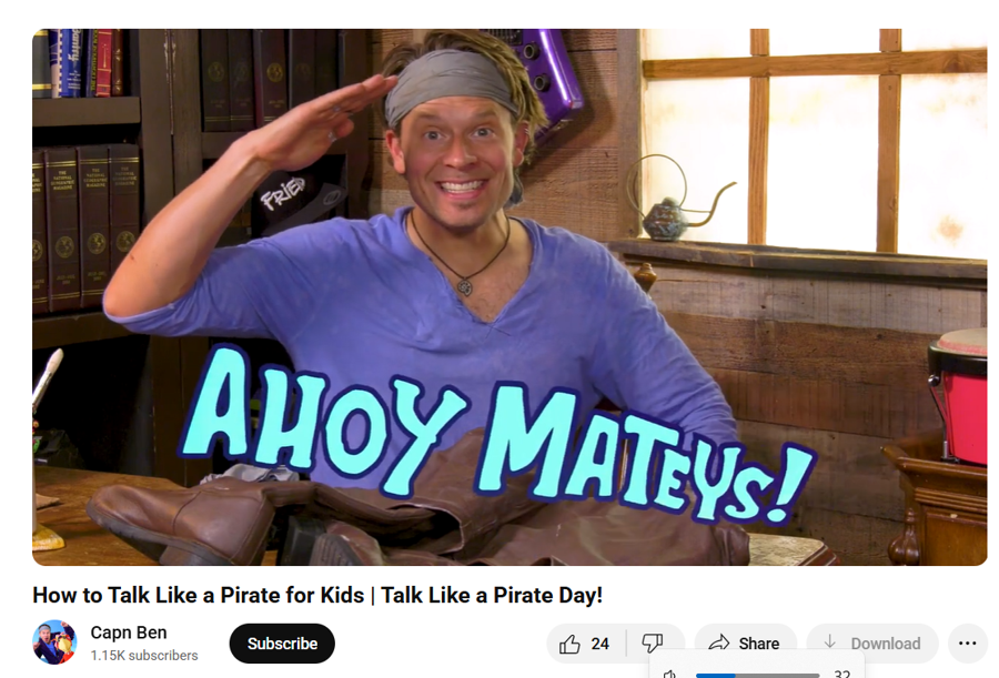 A man in a blue shirt and headband happily greets viewers with the phrase 'AHOY MATEYS!' in vibrant letters, set against a rustic backdrop.